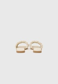 Sandales beige clair avec des brides tressées, semelle plate et design minimaliste. Texture douce et finition sans couture pour un confort optimal.