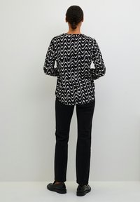 Maglietta a maniche lunghe bianca e nera con un motivo ondulato, abbinata a pantaloni neri slim-fit e scarpe nere. Vista di schiena.