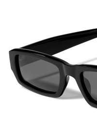Black sunglasses with a wide, angular frame; dark lenses; smooth plastic texture; thick temples; minimal detailing and accents.