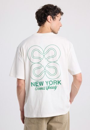 Cream-colored cotton t-shirt with short sleeves. Features a green graphic design of interlocking shapes and the text "NEW YORK Tennis Society" on back.