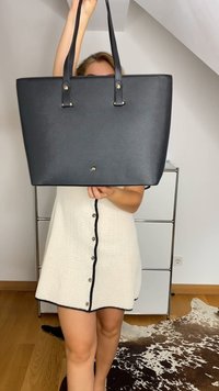 Saco tote preto com acabamento texturizado, alças duplas e acessórios em dourado. Apresenta um formato retangular espaçoso e design minimalista.
