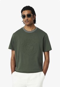 Groen T-shirt met korte mouwen en een cirkelvormig reli�ëflogo, met een gestreepte halslijn. Gemaakt van zachte stof en heeft een comfortabele pasvorm.