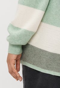 Črtast pleten pulover v svetlo zeleni, kremni in sivi barvi. Ima rebraste manšete in teksturiran zaključek, ki prikazuje različne vodoravne črte.