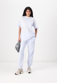 Light blue cotton t-shirt with relaxed fit, paired with matching light blue sweatpants. Gray Nike fanny pack and beige sneakers complete the look.