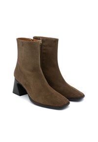 Botines de ante marrón con punta afilada, detalle de cremallera dorada y tacón negro grueso. Textura suave con adornos mínimos.