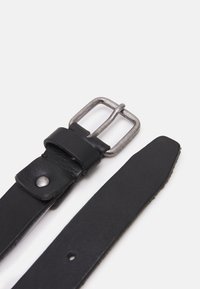 Svart lærbelte med en metallspenne. Spennen er rektangulær med en svak tarnish. Beltet har en glatt tekstur uten synlige mønstre.