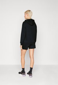 Sweatshirt preto com capuz, combinado com calções pretos. Apresenta um detalhe texturizado no decote. Usado com sapatilhas pretas e meias.