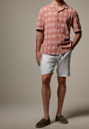 Kurze, kariertem Hemd in sanftem Pink, kombiniert mit weißen Shorts. Getragen mit braunen Slippern, zeigt ein entspanntes Sommeroutfit.