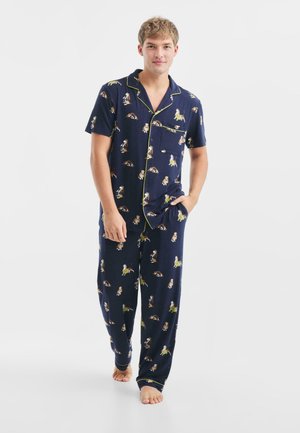 Marineblåt pyjamas sæt med kortærmet skjorte og lange bukser, har legende dyremønstre, kontrasterende gul kant og blødt stof.