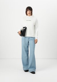 Felpa bianca con logo "Calvin Klein", abbinata a jeans a gamba larga di un azzurro chiaro e a una borsa geometrica nera. Tessuto morbido, vestibilità rilassata.