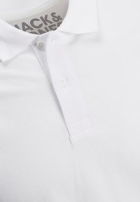 Polo shirt blanc en tissu tissé avec une patte de boutonnage à deux boutons et un col texturé. Comprend une étiquette de marque à l'intérieur du col.