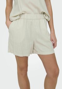 Beige linnen shorts met een elastische tailleband en zijzakken. De stof heeft een subtiele textuur en een relaxte pasvorm, die eindigt boven de knie.