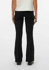 Pantalon flare noir en tissu extensible. Présente une texture lisse avec une taille haute et un ourlet évasé, vu de dos.