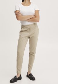 Beige skräddarsydda byxor med en elegant design och en mjuk yta. Bärs med en tajt vit t-shirt och svarta loafers.