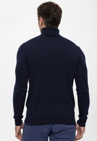 Granatowy sweter z golfem, wykonany z prążkowanej dzianiny, z długimi rękawami i dopasowanym krojem, o fakturowanej powierzchni i bez widocznych wzorów.