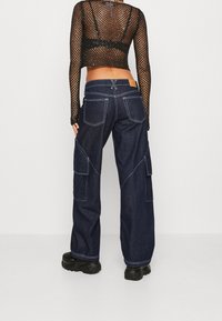 Mörkblå denim cargo-byxor med flera fickor, kontrasterande sömmar och en avslappnad passform. Matchas med en svart nättröja med lång ärm.