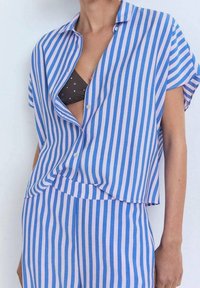 Chemise à manches courtes à carreaux bleus et roses, avec une coupe décontractée, associée à un short assorti. Le matériau semble léger et doux.