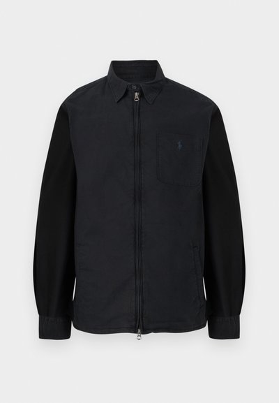 Zwarte lange mouwen overhemdjas met een rits aan de voorkant, een kraag met knopen en een borstzak met een klein geborduurd logo.