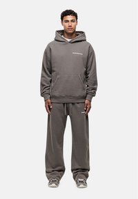 Felpa grigia in cotone con tasca a marsupio e logo bianco, abbinata a pantaloni della tuta a vestibilità rilassata e sneakers grigie.