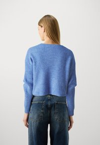 Modrý pletený sveter s krátkym strihom a rebrovanou štruktúrou, skombinovaný s tmavými džínami s vysokým pásom a zadnými vreckami.