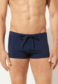 Navyblaue Badehose mit einem elastischen Bund und Kordelzug. Glatter, dehnbarer Stoff mit minimalen Nähten und ohne zusätzliche Muster.
