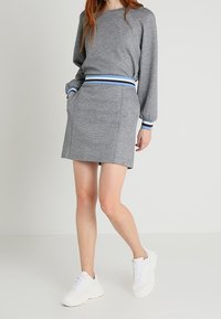 Sweatshirt gris avec une ceinture rayée bleue et marron, associé à une jupe grise assortie. Des baskets blanches complètent l'ensemble.