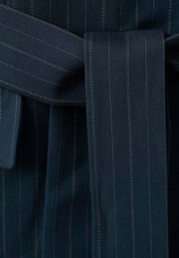 Tissu bleu foncé avec de fines rayures verticales blanches noué en un nœud plat, montrant la texture et les détails de couture.