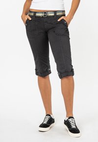 Zwarte capri-broeken met omgeslagen zoom, zijzakken en decoratieve knopen. Gecombineerd met een meerkleurige gestreepte riem en zwarte sneakers.