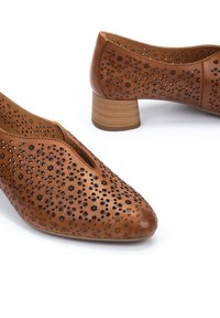 Chaussures en cuir marron avec des motifs de fleurs découpés, un bout pointu et un petit talon en bois. Texture lisse avec un design perforé.