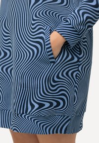Abito blu a fantasia con linee ondulate in diverse tonalità, dotato di tasche laterali e polsini a coste. Il materiale sembra morbido ed elastico.