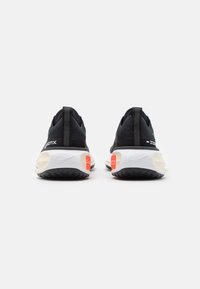 Chaussures de sport noires avec une tige en maille texturée, une semelle intermédiaire blanche et des accents orange contrastants sur le talon et le côté.