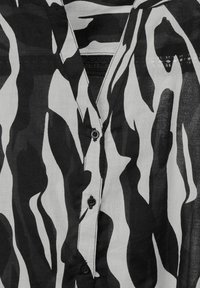 Camicia bianco e nero con motivo a onde, dotata di abbottonatura frontale, colletto e dettagli in tessuto testurizzato vicino al collo.