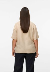 Beige kortærmet skjorte med struktureret finish, løs pasform og rund kant. Båret sammen med mørke denimbukser, set fra ryggen.