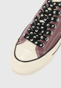 Burgundy vászon sneaker fekete yin-yang mintázatú fűzőkkel, krém színű orr résszel és fekete gumis szegéllyel. Fehér varrási részletekkel rendelkezik.