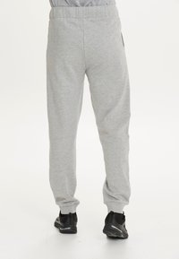 Graue Sweatpants aus weichem Material, mit einem elastischen Bund und schmal zulaufenden Beinen. Kombiniert mit schwarzen Sportschuhen für einen Kontrast.