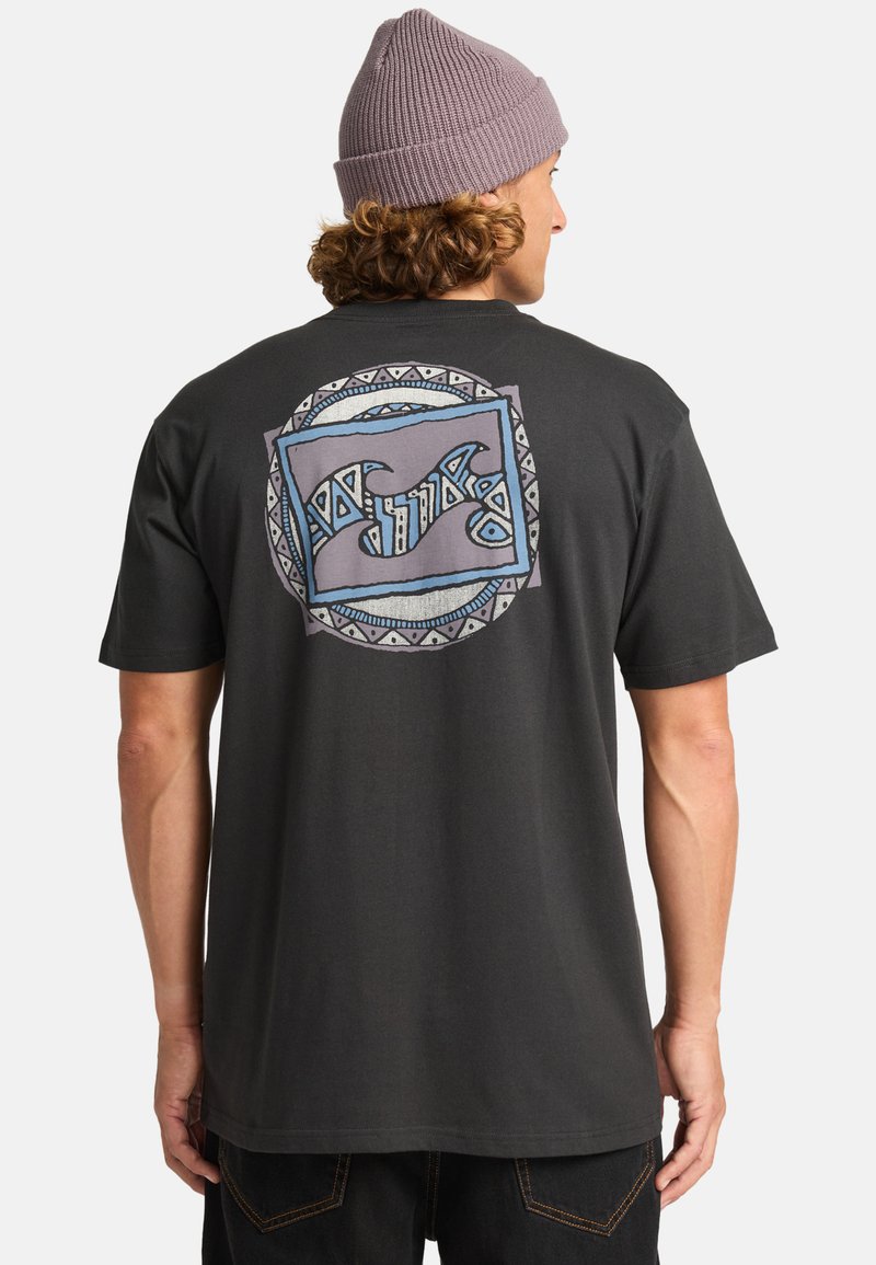 Svart bomull T-skjorte med bakre grafikk som viser abstrakte bølger og geometriske mønstre i blått og grått. Modellen har på seg en lavendel lue.