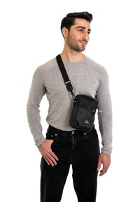 Borsa a tracolla nera realizzata in nylon con fronte texturizzato, chiusura con zip, tracolla regolabile e piccolo logo dettagliato nella parte inferiore.