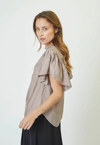 Blusa beige chiaro a maniche corte con texture morbida e motivo a righe sottili. Presenta maniche con rouches e scollatura rotonda.
