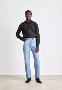 Črna srajca s gumbi, svetlo modri naravnost krojeni jeans in črne gležnjarje. Gladek material s klasičnim krojem in diskretnimi podrobnostmi.