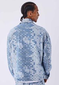 Chaqueta vaquera con un patrón pixelado azul, cuello estándar, mangas largas y un corte holgado. El material es ligero y con textura.