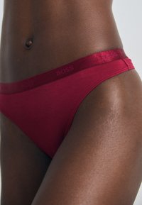 Rode bikini slip met een zachte textuur, voorzien van een satijnen afwerkingsband met de opdruk "BOSS." Ontworpen voor een strakke pasvorm met minimale bedekking.
