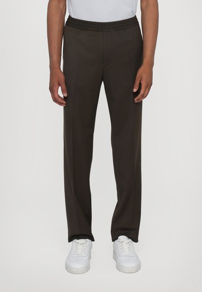 Pantalons marron foncé avec une taille élastique, coupe droite et léger éclat, associés à des baskets blanches.