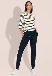 Gestreepte top in wit en zwart met driekwart mouwen, gecombineerd met marineblauwe joggers met een elastische tailleband en zakken. Witte sneakers.