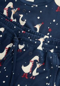 Navy blue pajama set featuring white geese in winter attire, accented with red and blue, with snowflakes and stars against the dark background.