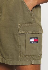 Olivgröna cargo shorts med fickdetaljer, prydda med en märkespatch i röd, vit och blå som framhäver Tommy Jeans-logotypen.