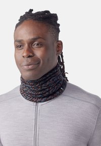 Tour de cou multicolore en tissu doux avec un motif abstrait. Porté serré autour du cou, associé à un haut zippé gris.