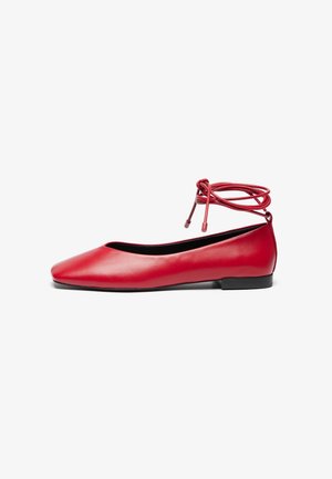 Chaussure plate en cuir rouge avec bout pointu et long lacet enveloppant la cheville, semelle noire, vue de côté sur fond blanc.