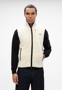 Ανδρικό γιλέκο σε κρέμ και μαύρο, με ψηλό γιακά, πλήρη φερμουάρ και δύο πλαϊνές τσέπες. Κατασκευασμένο από μαλακό ύφασμα με το λογότυπο της ομάδας στο στήθος.