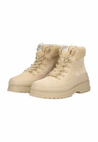 Beige suède enkellaarsjes met faux fur voering, ronde neus, dikke zool, acht metalen oogjes en merklabels op de tong.