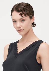 Top negru fără mâneci, cu decolteu în V, având o dantelă decorativă pe marginea decolteului. Material neted cu un luciu subtil.